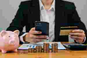 Mann mit Smartphone, Bankomatkarte, Sparschwein und Münzen